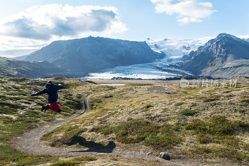 Man jumping in Kvíármýrarkamkur valley with a glacier tongue at the background in iceland.